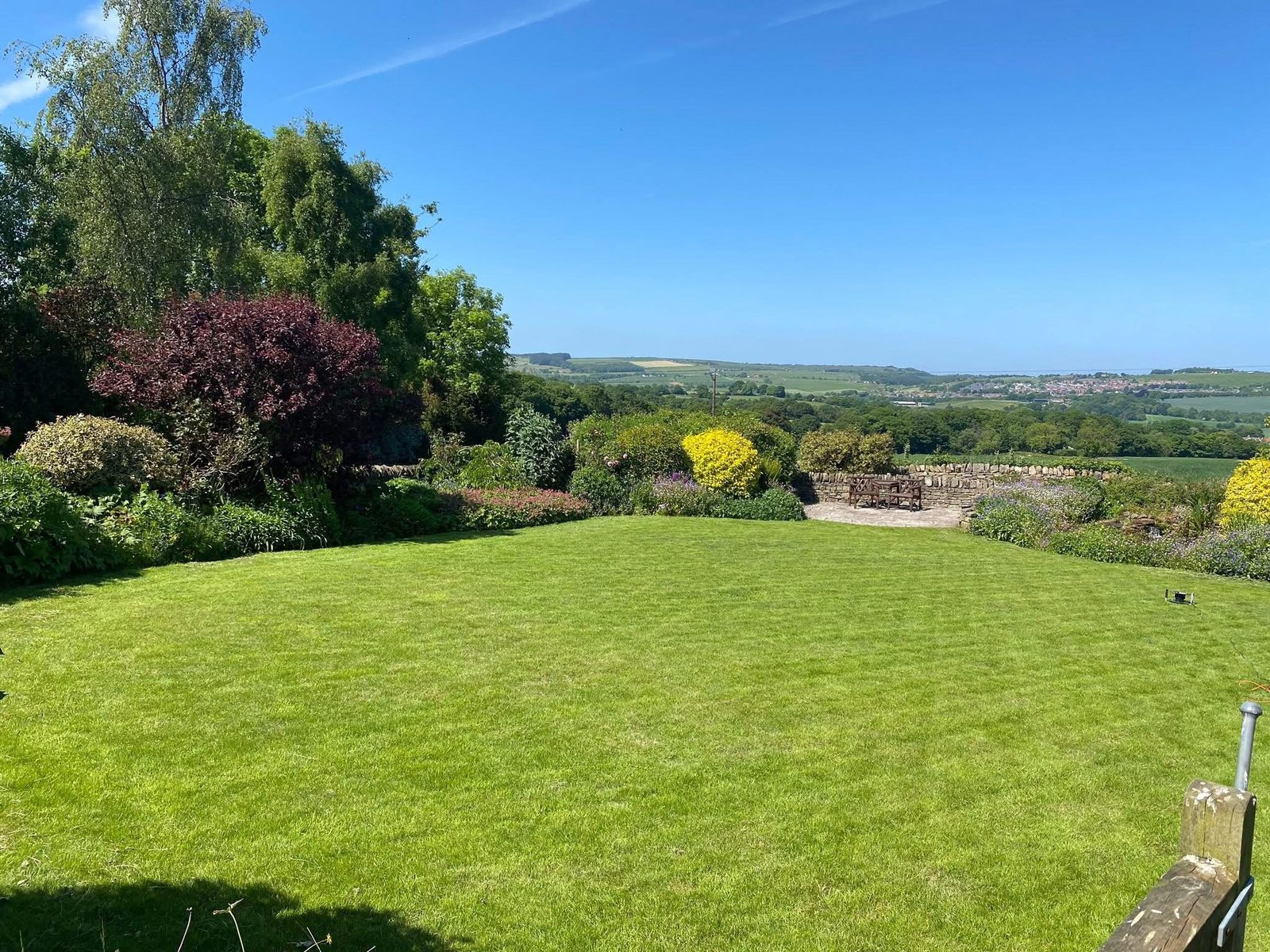 A freshly mown, striped lawn with mature borders and a view over the countryside