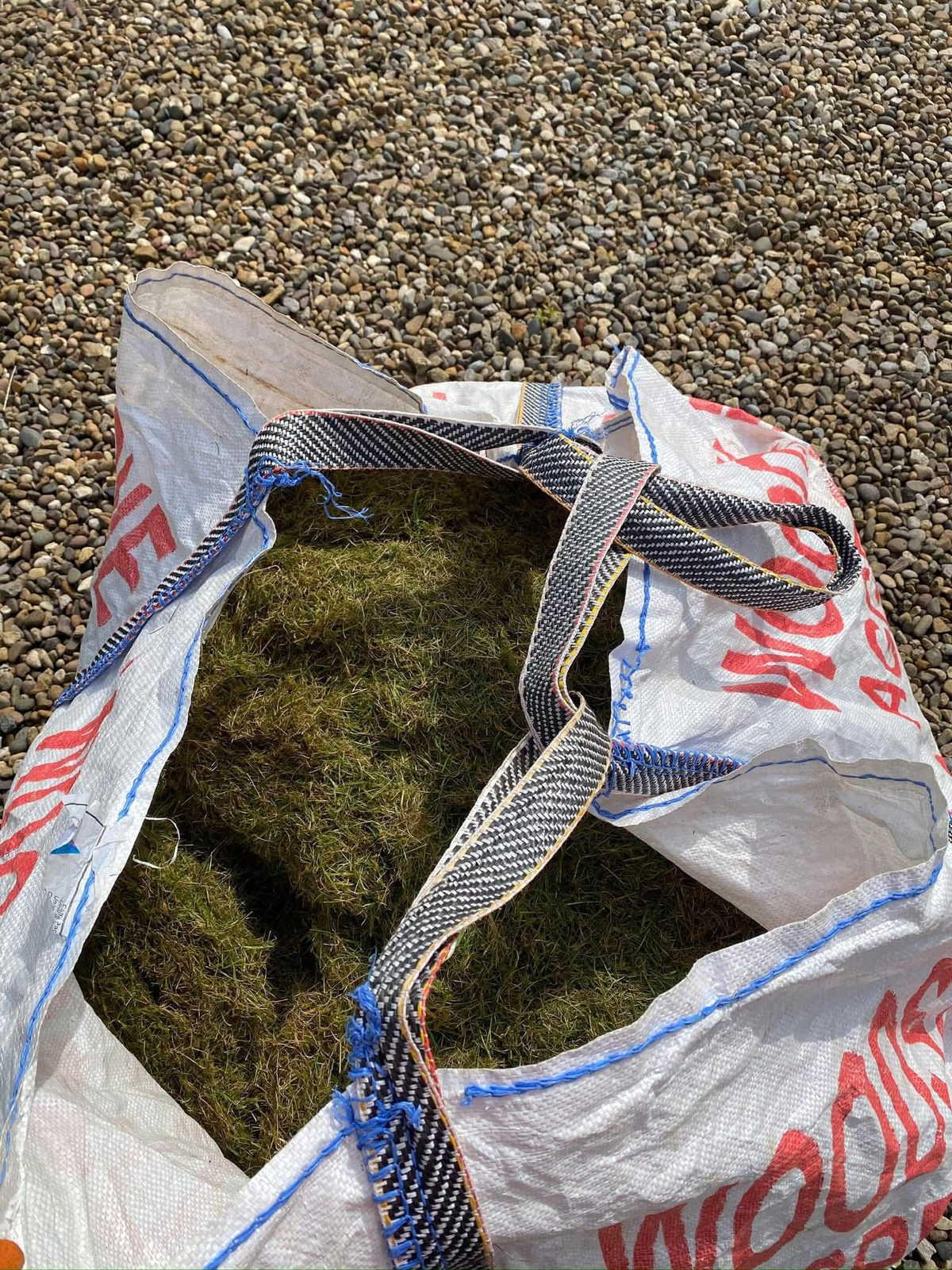 A second bag of raked-out thatch standing on a gravel drive