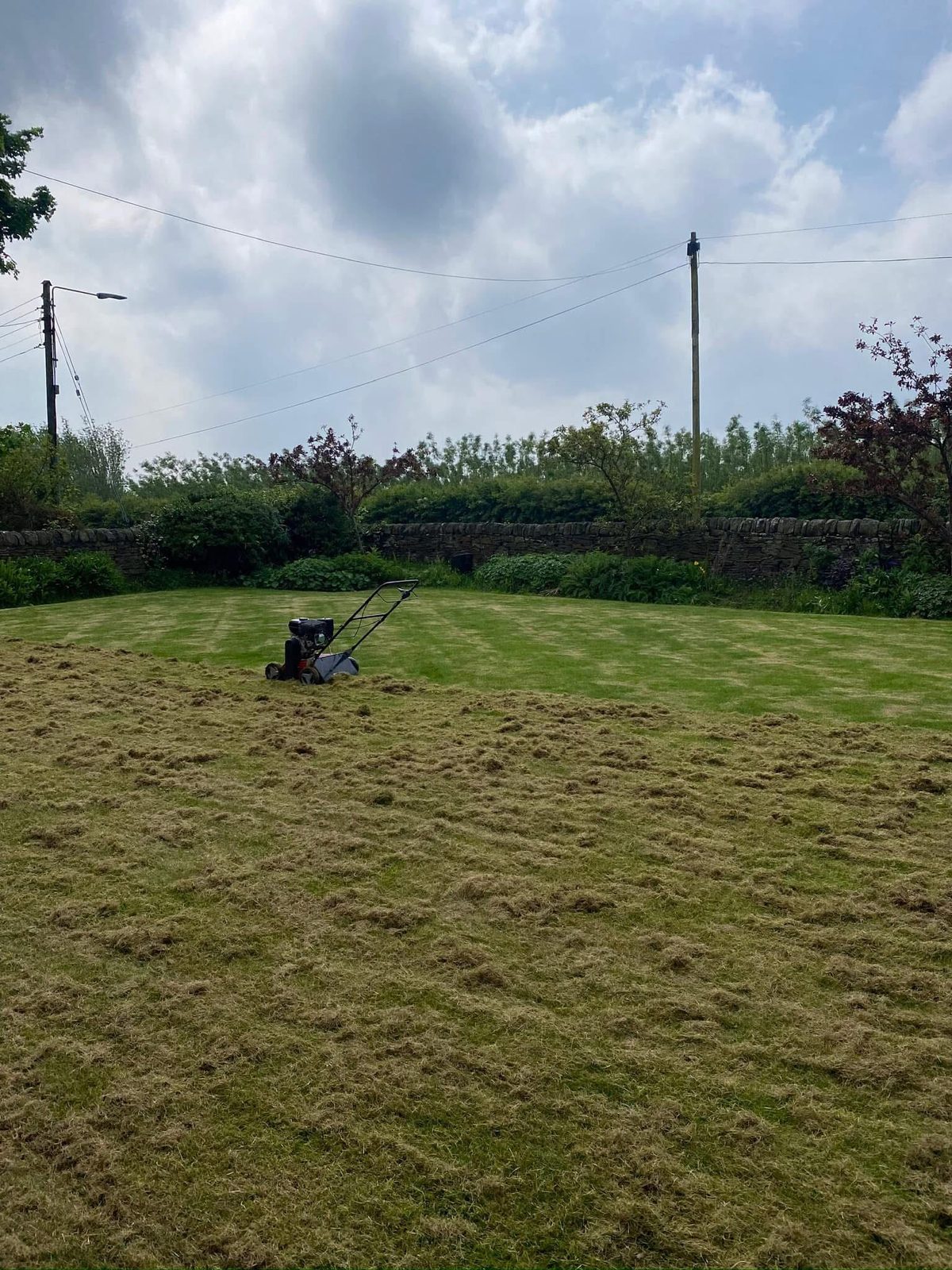 A lawn mid-job with a mower parked on it and a freshly finished stripe of grass